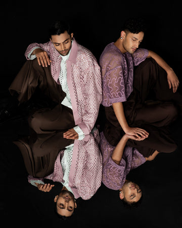 ROSANI Guarded Beauty campaign - two models in lace-textured tops in blush pink and violet with dark trousers on a black background, mirrored reflection composition