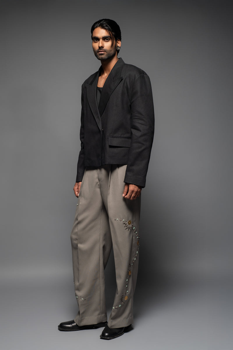 ROSANI The Kichka trouser in stone grey - wide-leg tailored trousers with floral thorn-inspired embellishment along the leg and elastic back waistband, side view, styled with a black blazer