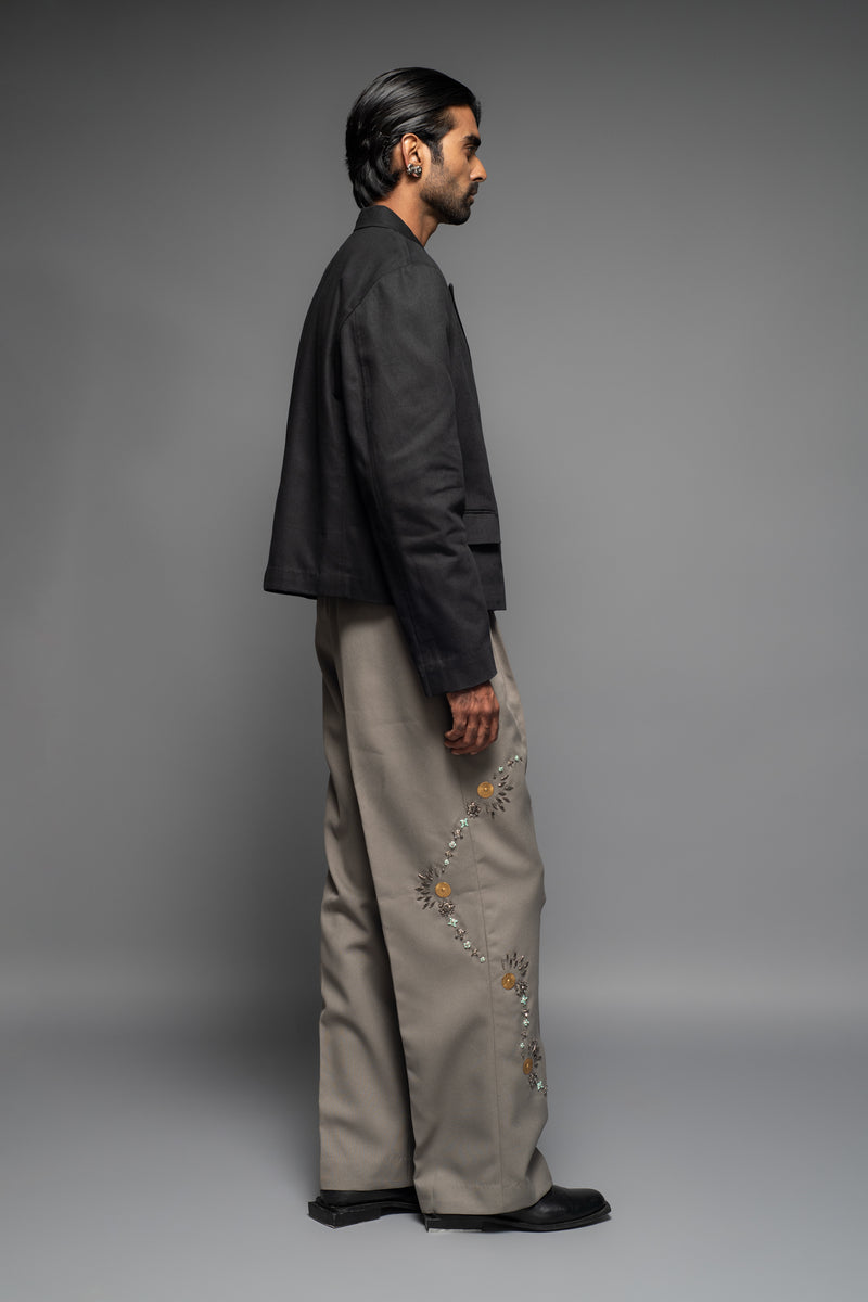 ROSANI The Kichka trouser in stone grey - wide-leg tailored trousers with floral thorn-inspired embellishment along the leg and elastic back waistband, side view, styled with a black blazer