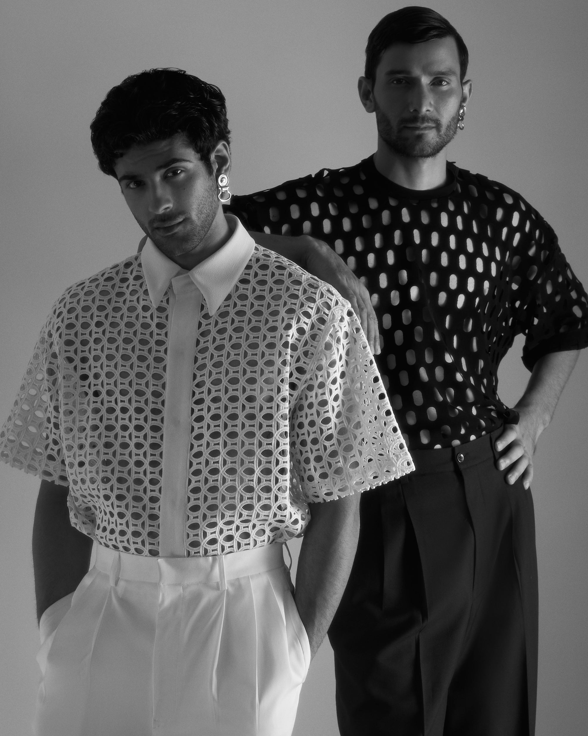 ROSANI DYMENSION collection image - two models wearing the Riflesso T-shirt with circular cut-out pattern, styled with high-waisted tailored trousers, black-and-white editorial front view