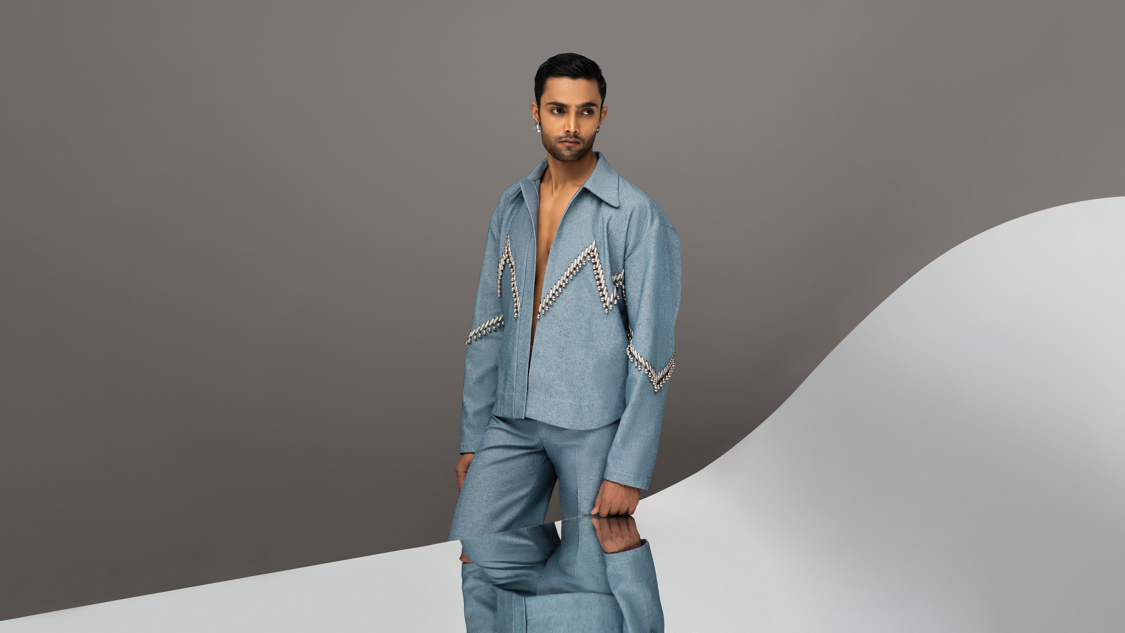ROSANI Guarded Beauty collection image - model wearing The Munzwa jacket in light blue denim with silver embellished zigzag detailing, paired with matching trousers, editorial front view