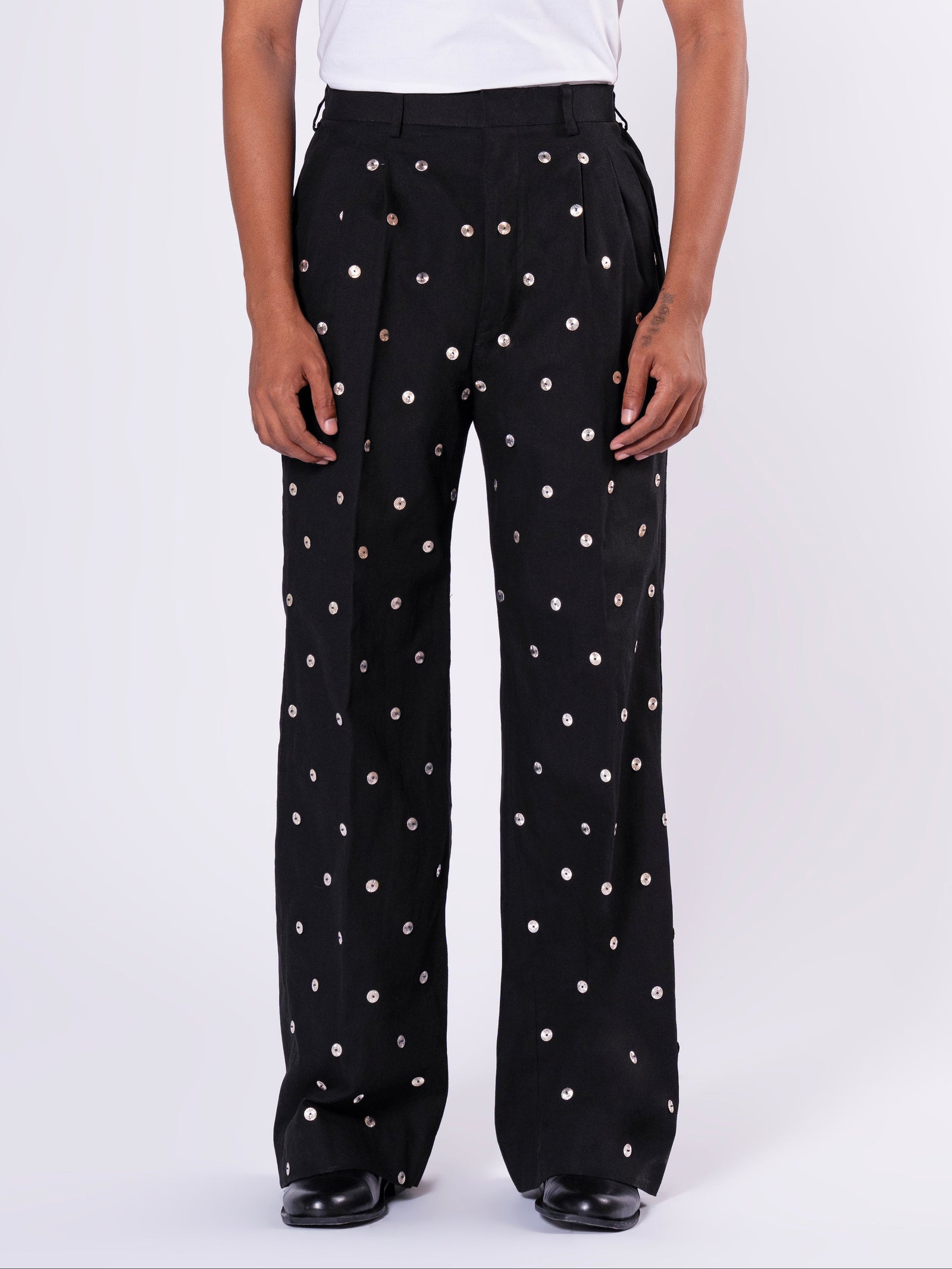ROSANI The Blythe trouser in black. Wide-leg pleated trouser with metallic disc embellishment and back elastic waistband. ANIMA and ANIMUS collection, front view.