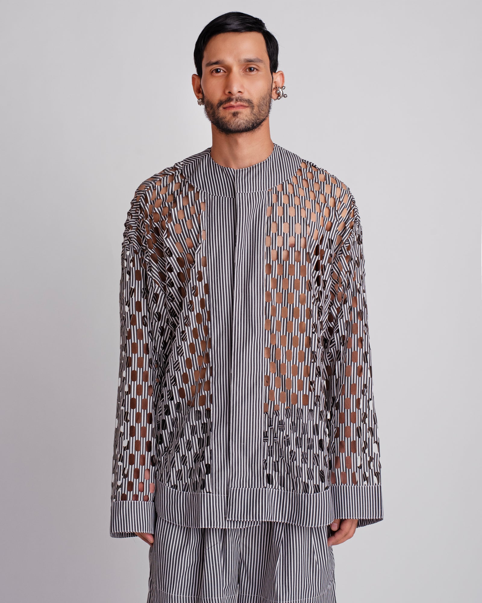 ROSANI The Emerson shirt in black and white stripes. Oversized laser-cut workwear shirt with metallic press buttons and geometric cut-out pattern. ANIMA and ANIMUS collection, front view.