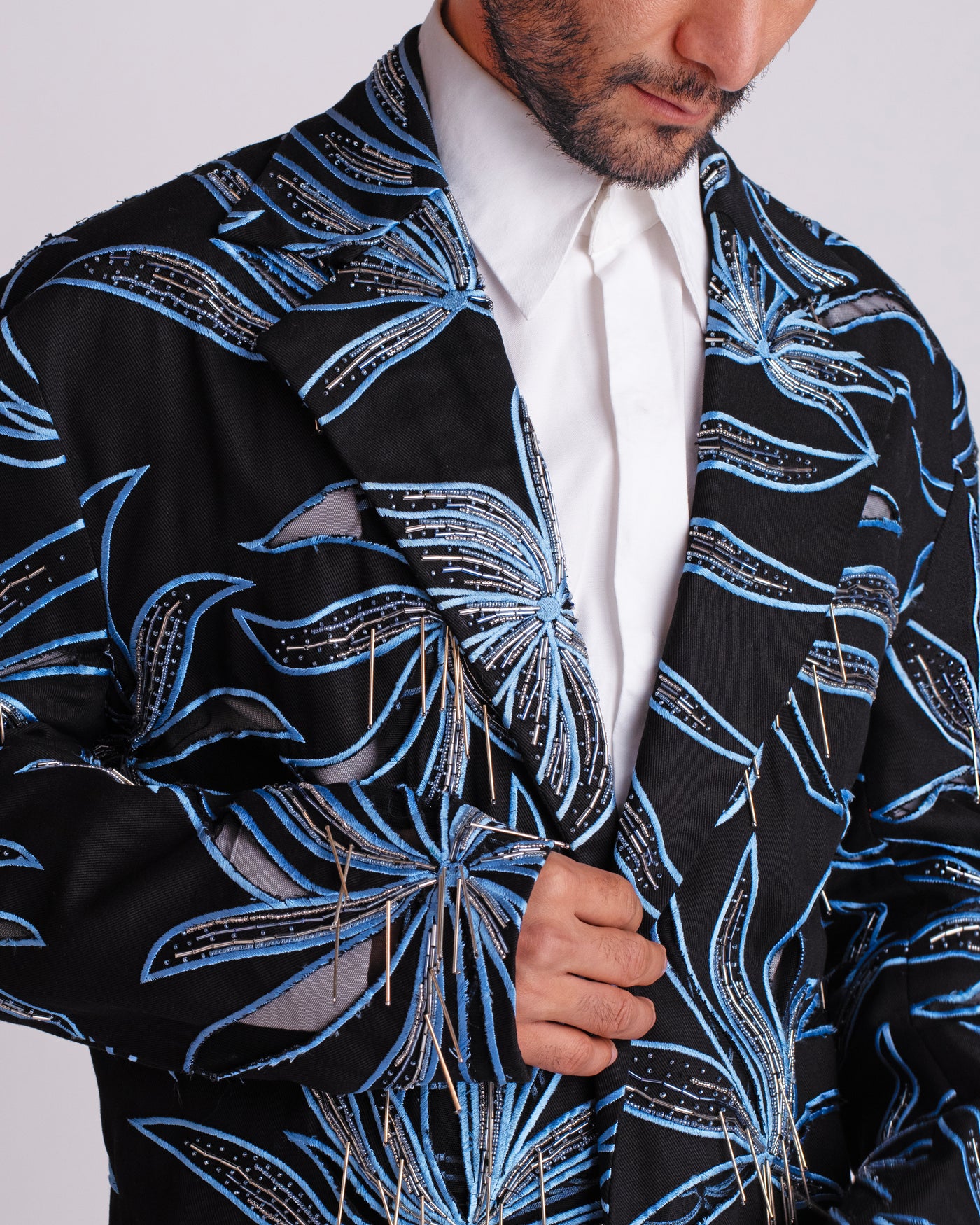ROSANI The Noah coat in black. Close-up of hand cutwork, thread embroidery and hanging glass rod detail.