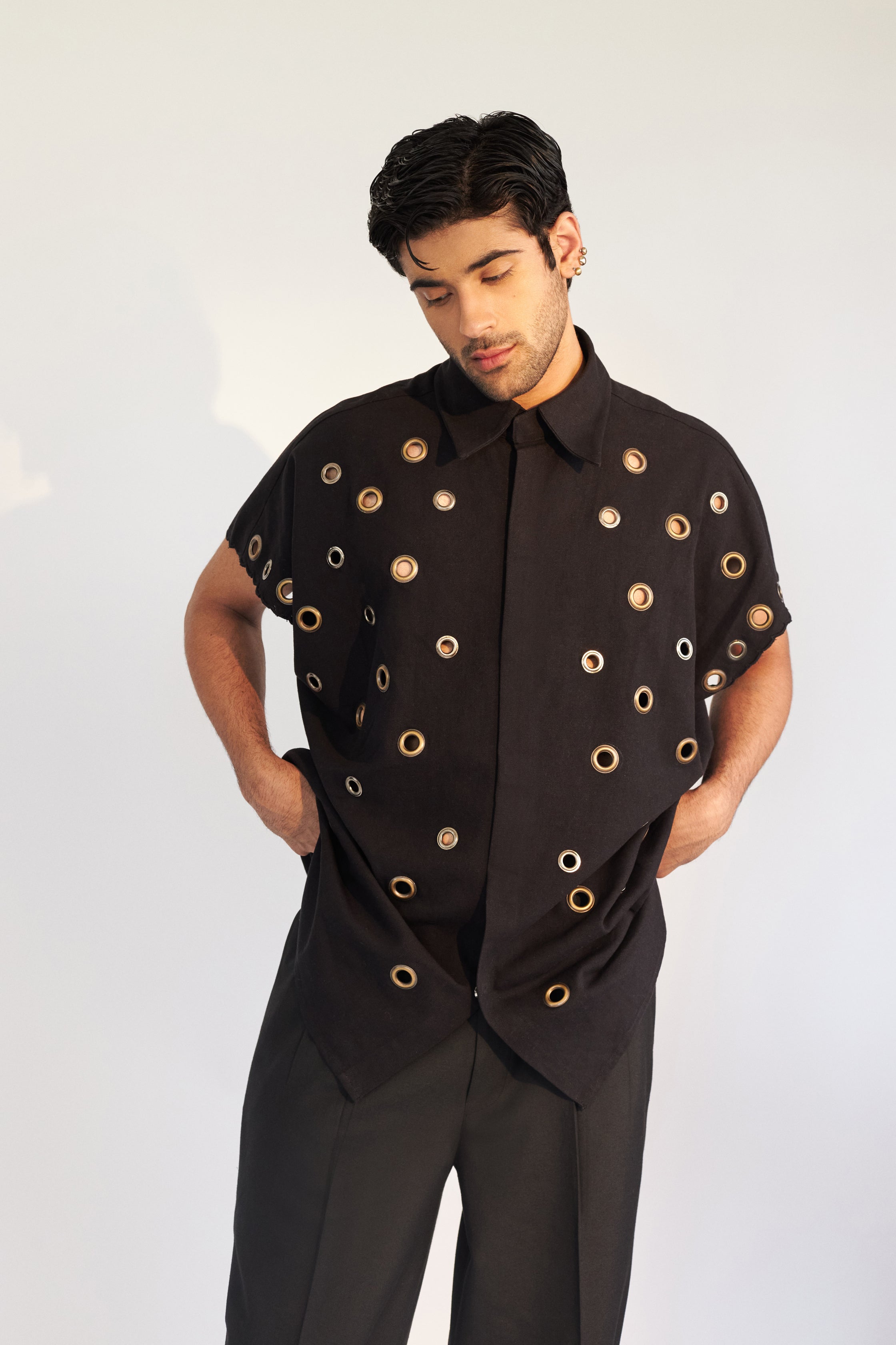 ROSANI The Le Franc shirt, front view. Oversized black cotton with all-over metal eyelets and snap button front. DYMENSION collection.